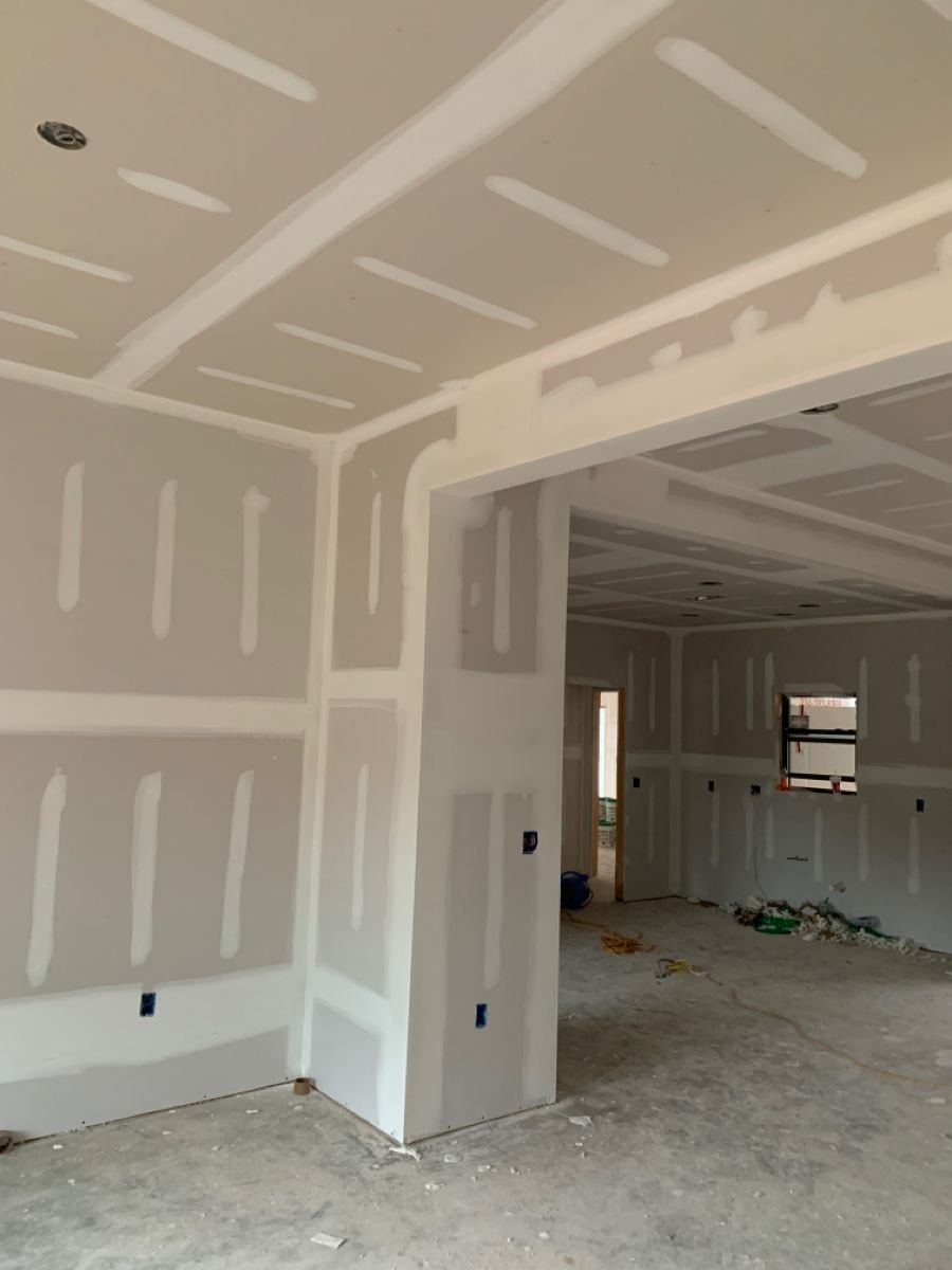 Interior under construction with taped and mudded drywall, open doorway, and construction debris on the floor