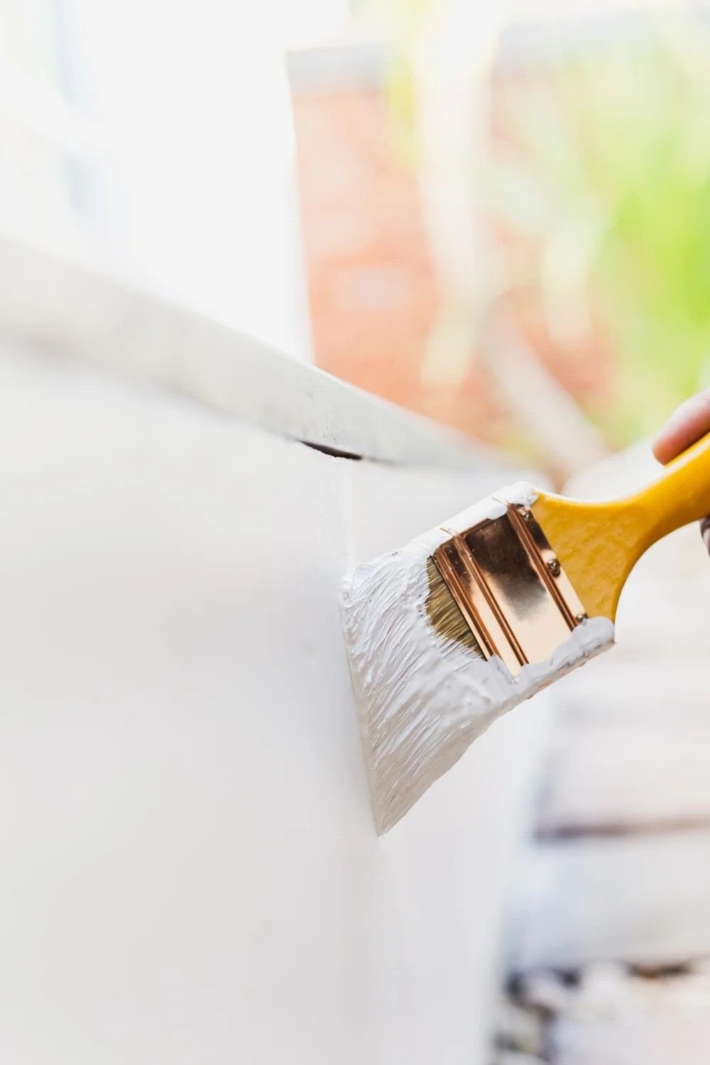 Close-up of a painter's brush applying white paint along the edge of a wall.