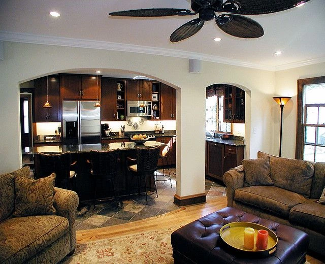 Open-concept living room and kitchen with dark wood cabinets, stainless appliances, and an island with bar stools on a tiled floor.